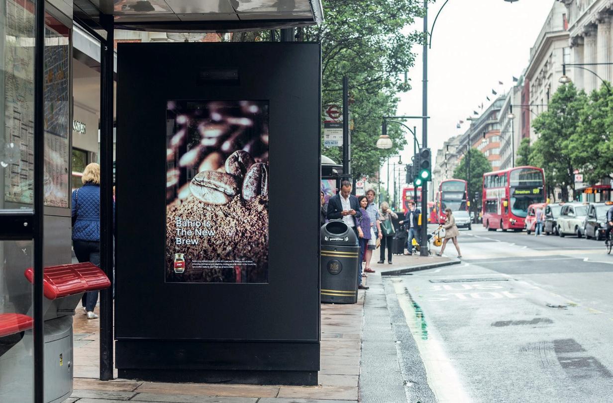 A Bahio coffee poster in a London bus shelter beside pedestrians and red buses.