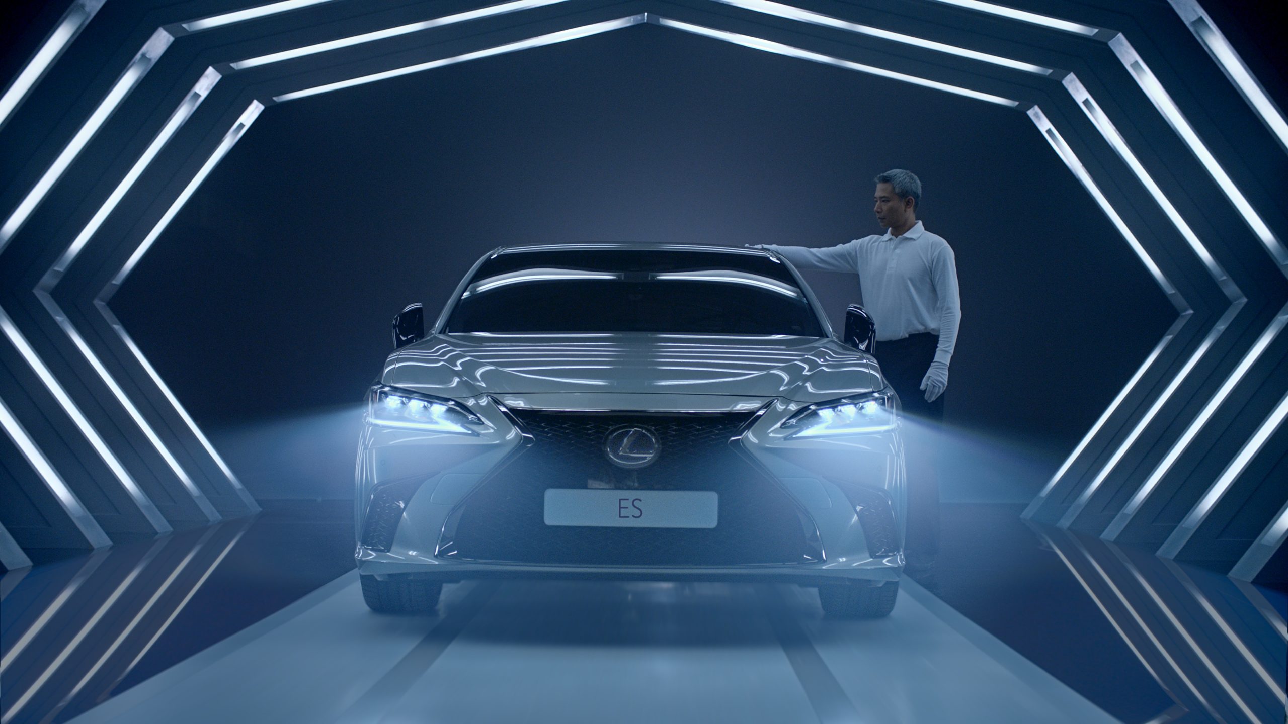 A Lexus ES under blue geometric lights with a craftsman standing beside the car.