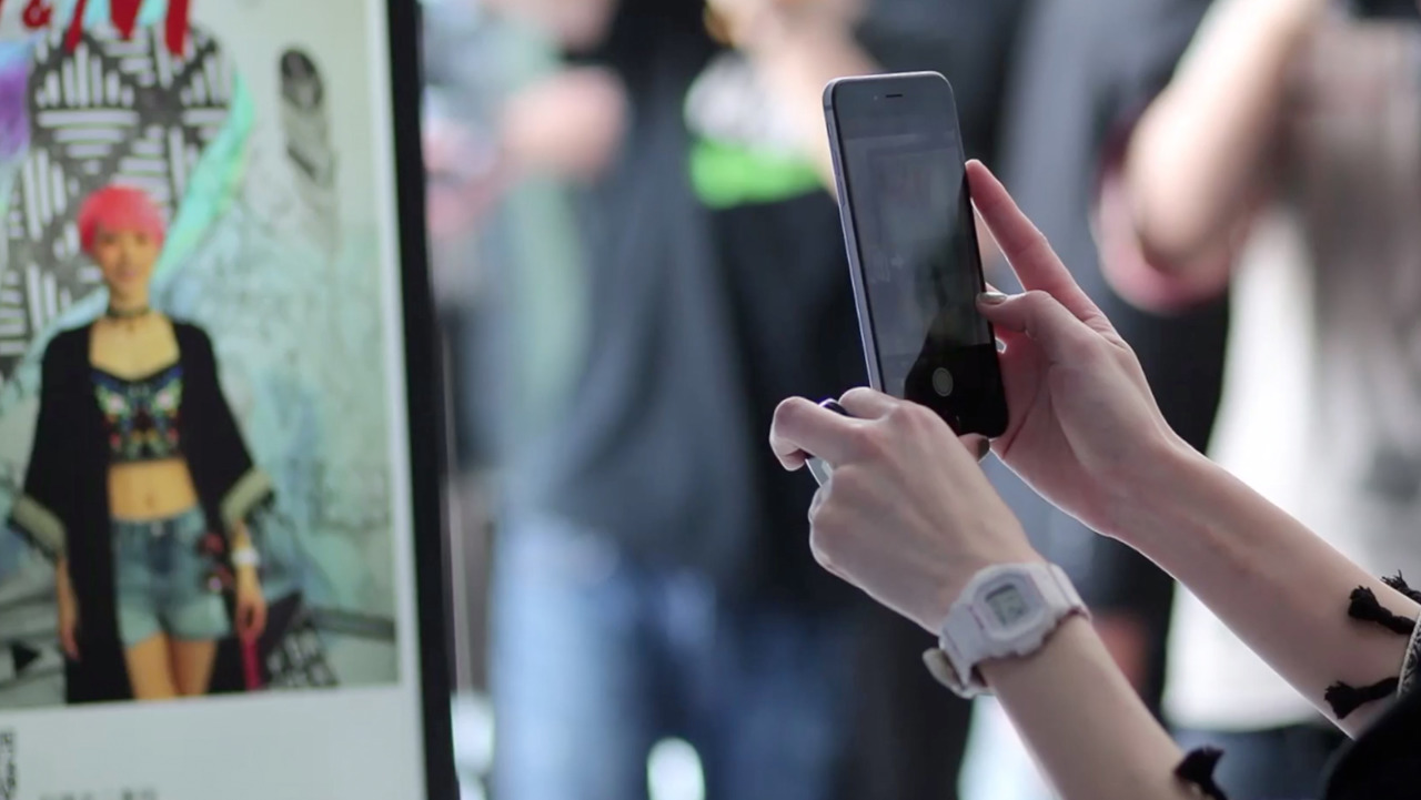 Person photographing an H&M street-style display with a phone.