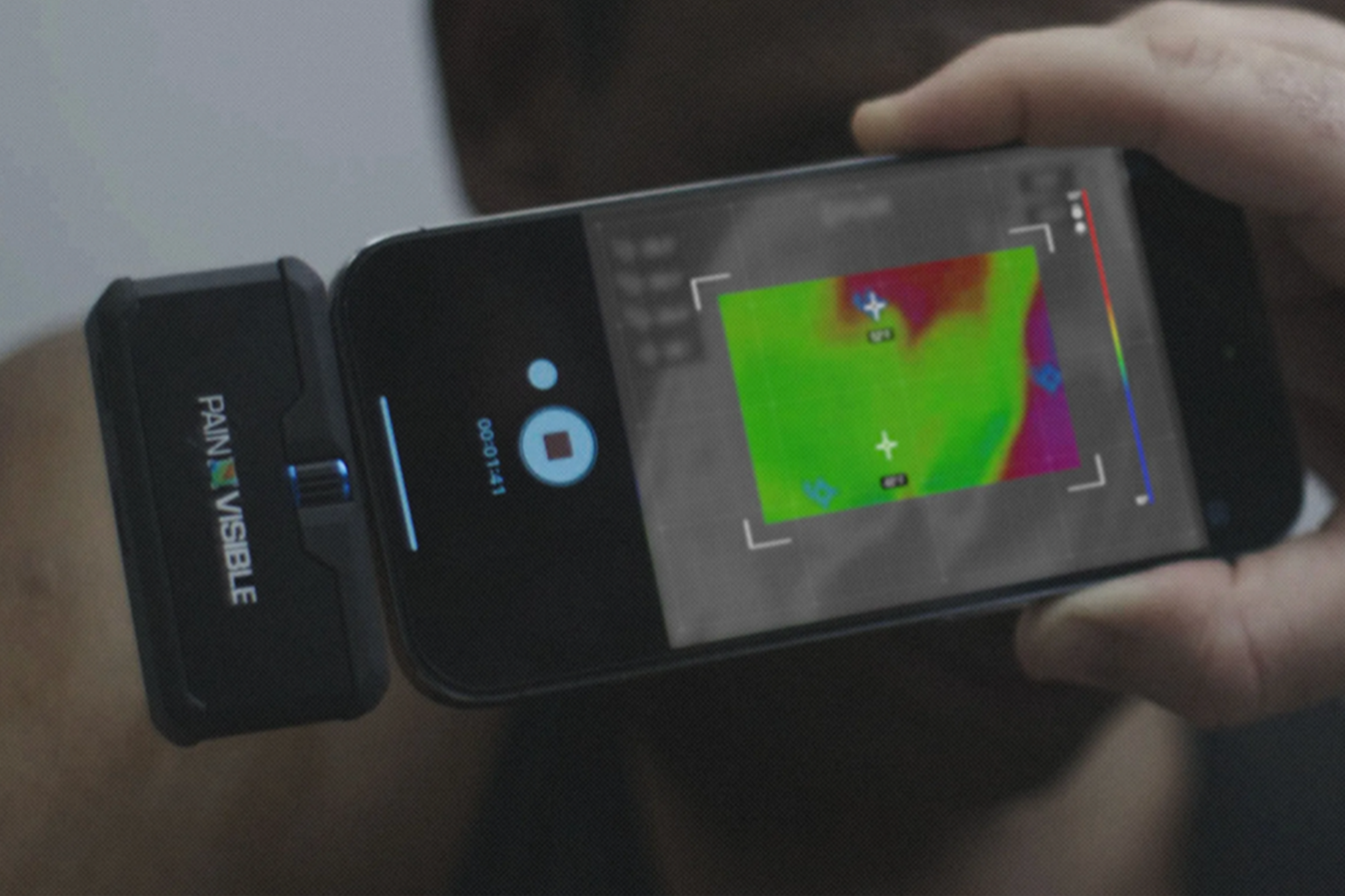 A handheld thermal camera and phone display a colored heat map.