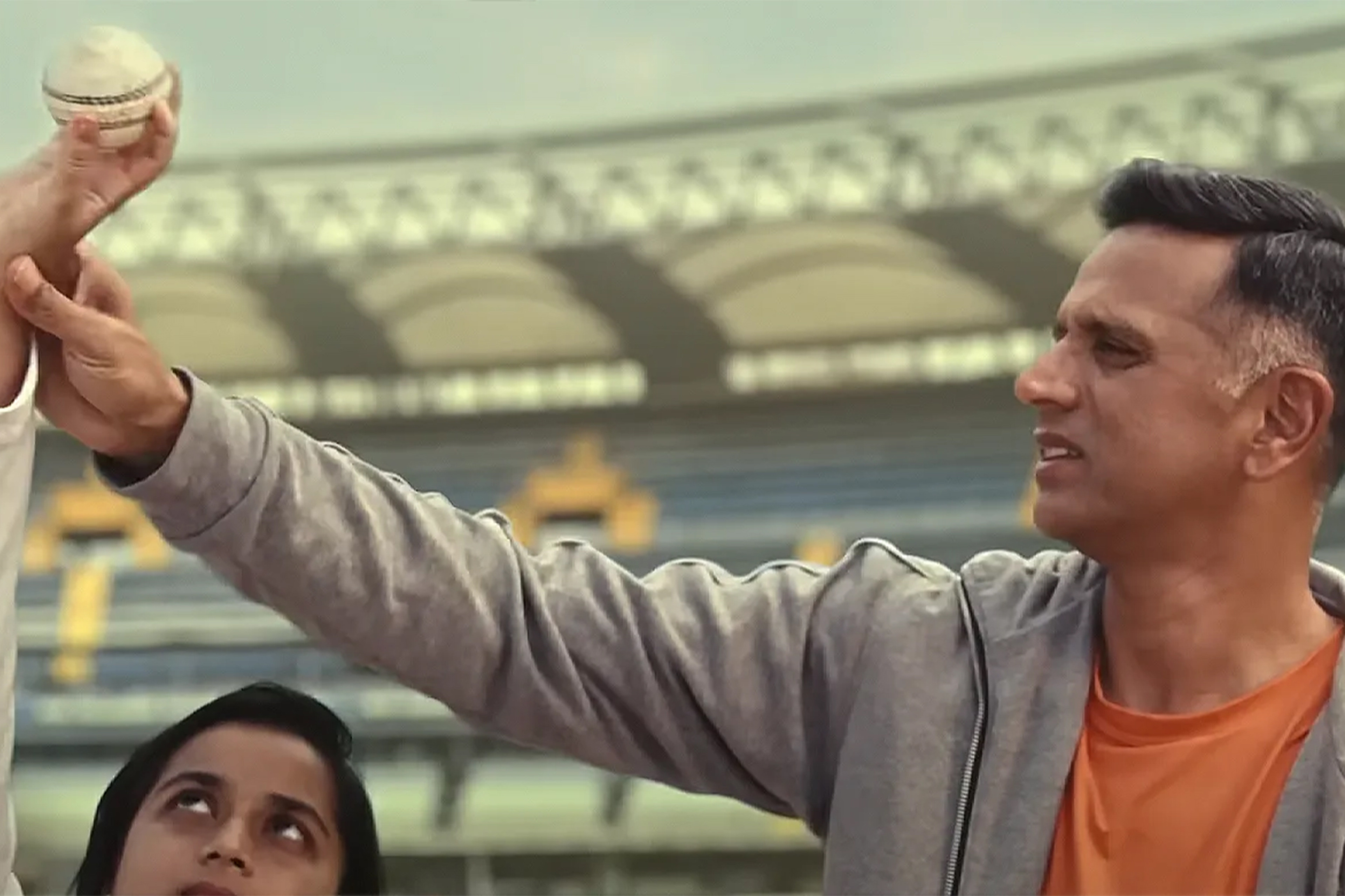 Rahul Dravid guides a child holding a cricket ball in a stadium.