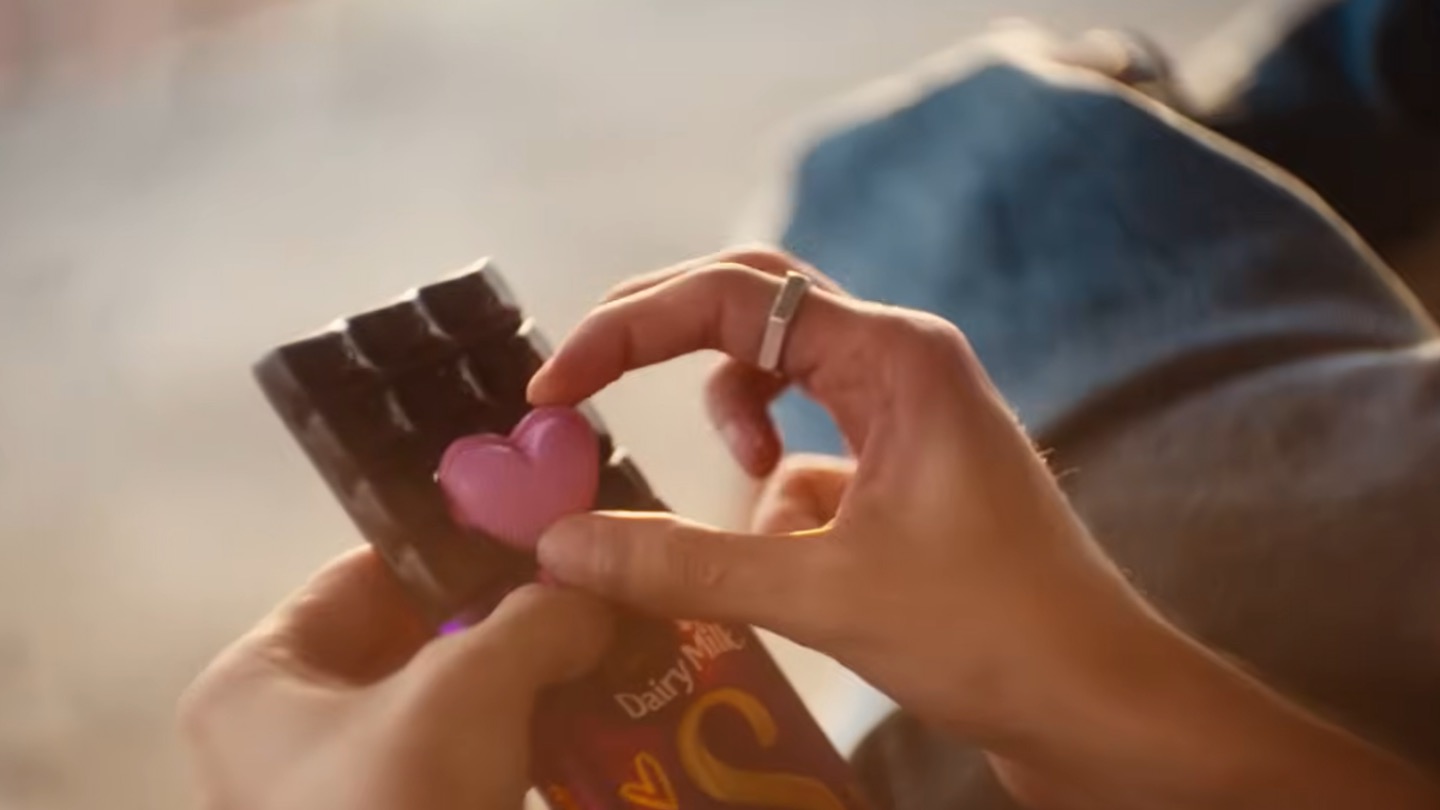 Hands hold Cadbury Dairy Milk Silk chocolate and a small pink heart-shaped object.