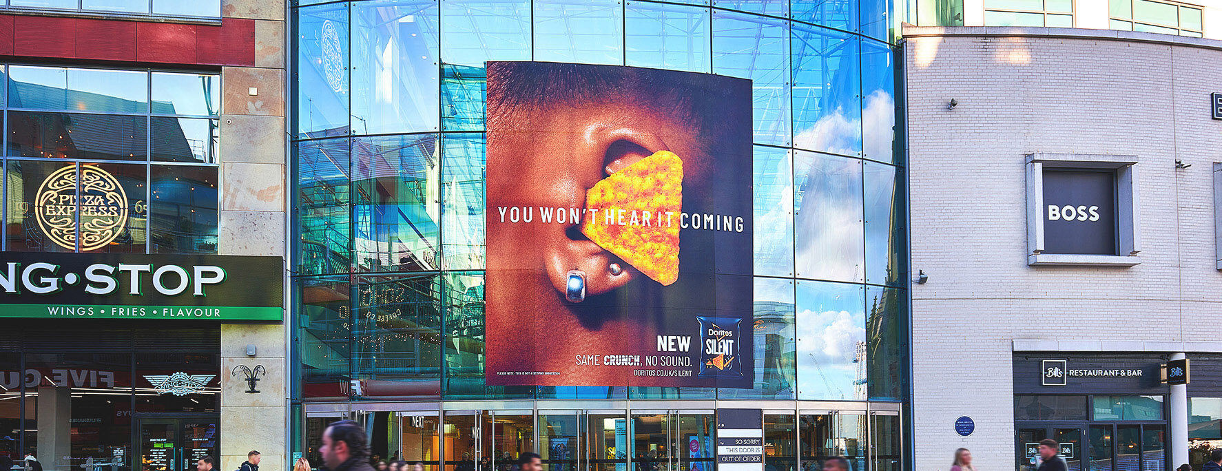 A large street billboard shows a person eating a Doritos chip beside the line ‘You won’t hear it coming.’
