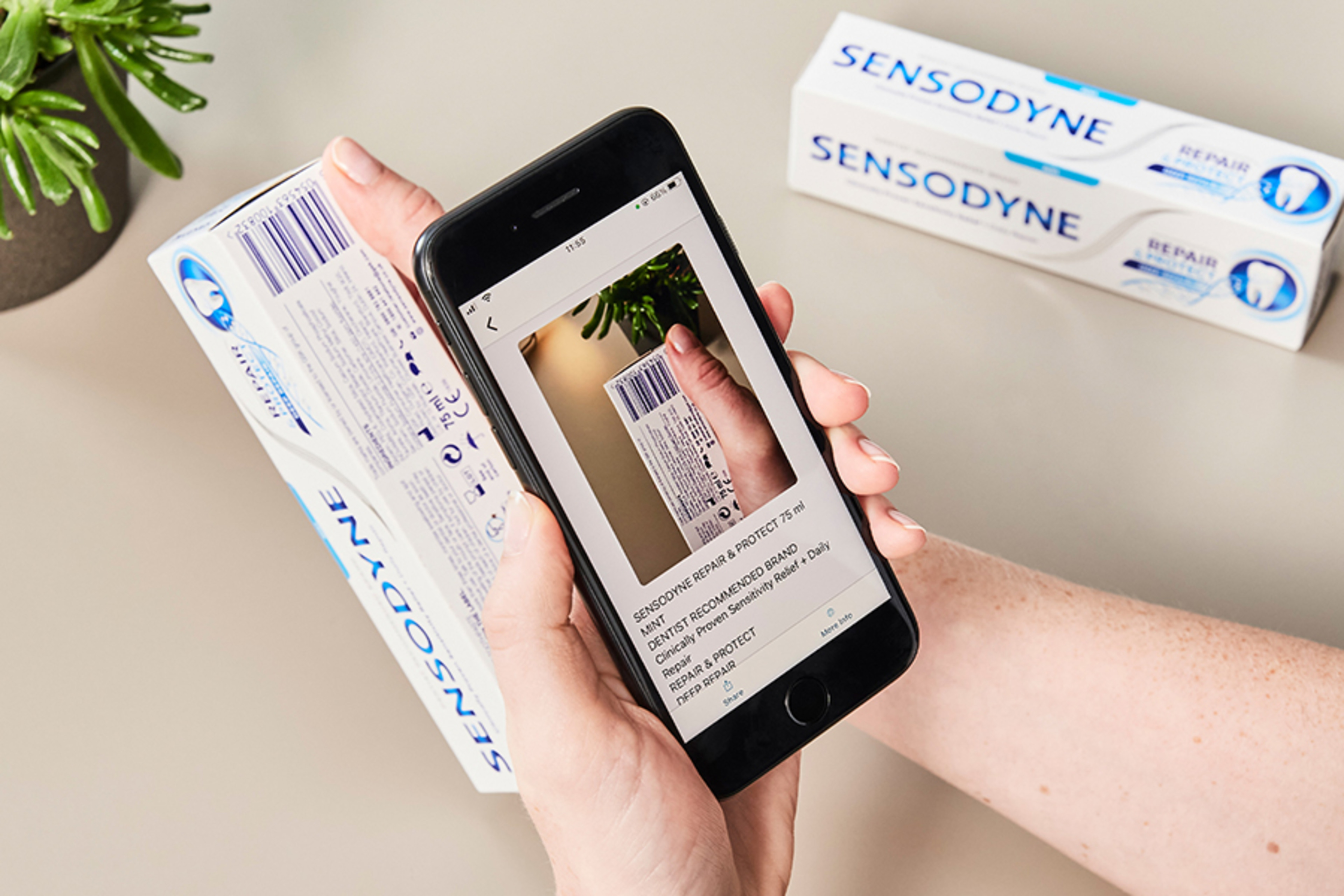 A phone scans the barcode of a Sensodyne toothpaste carton.
