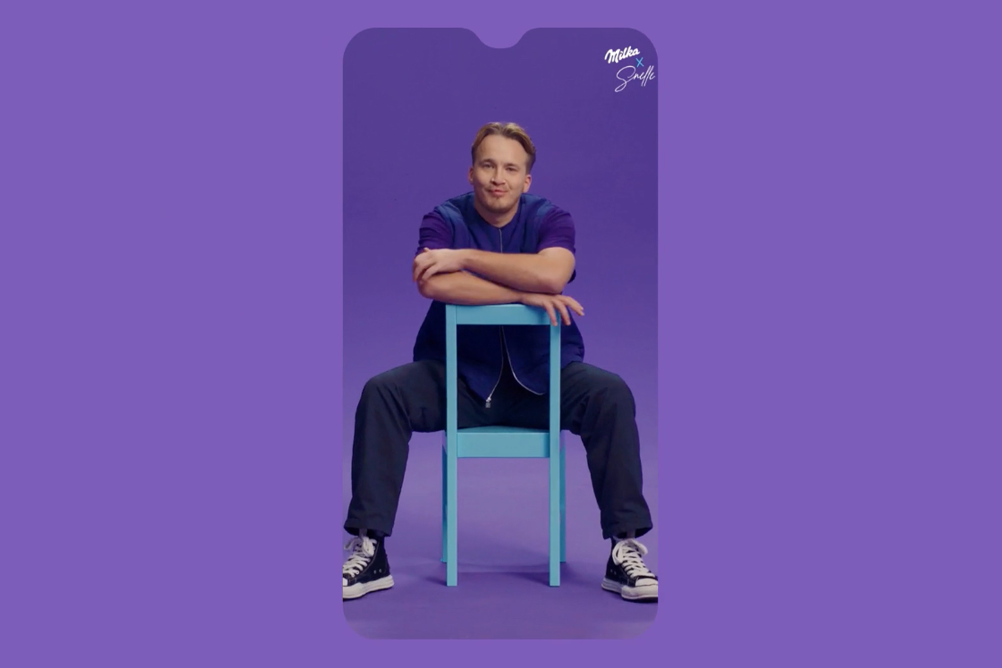 Dutch musician Snelle sits backwards on a blue chair inside a purple Milka-branded phone frame.