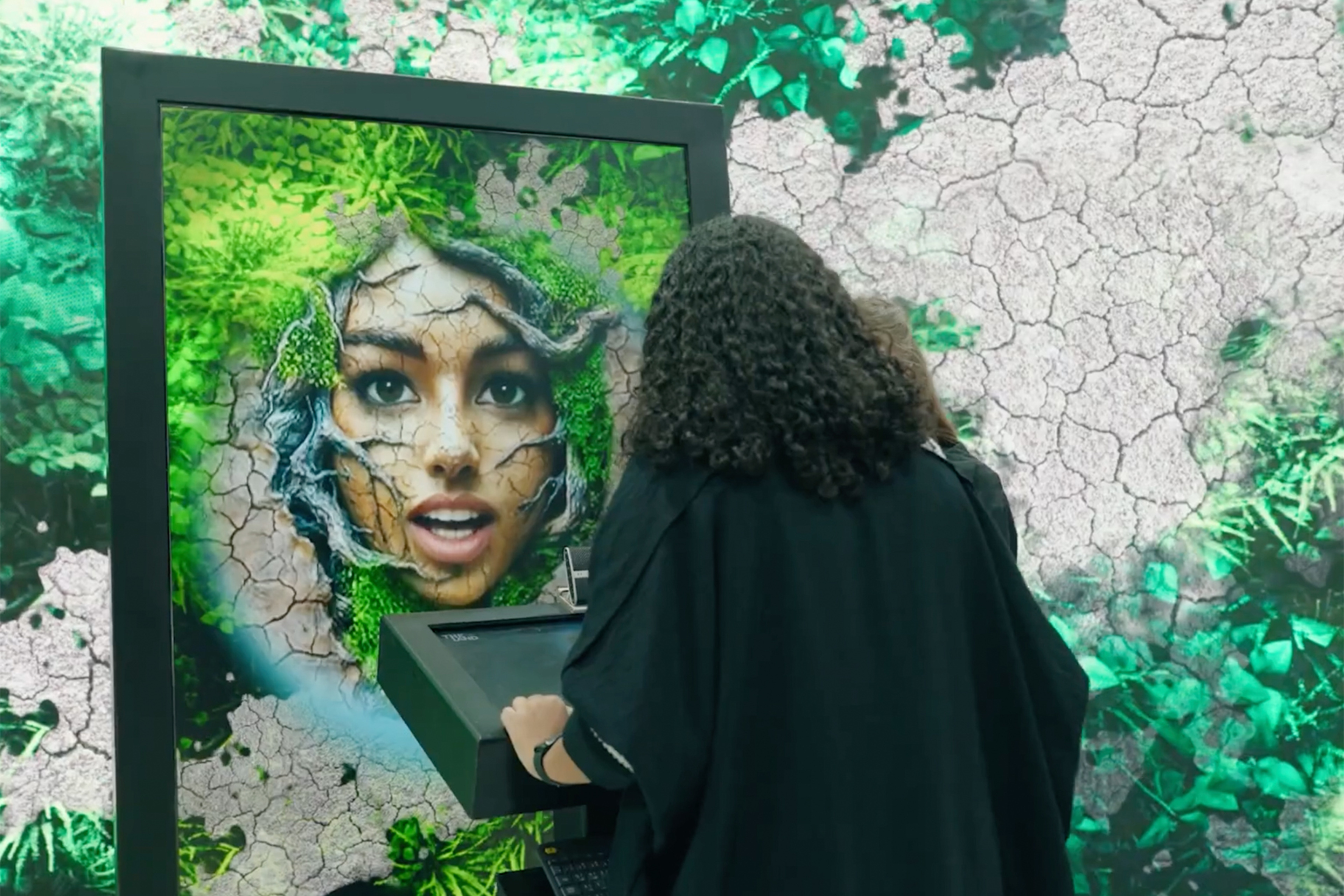 Visitor engages with a display portraying a human face fused with cracked soil and vegetation.