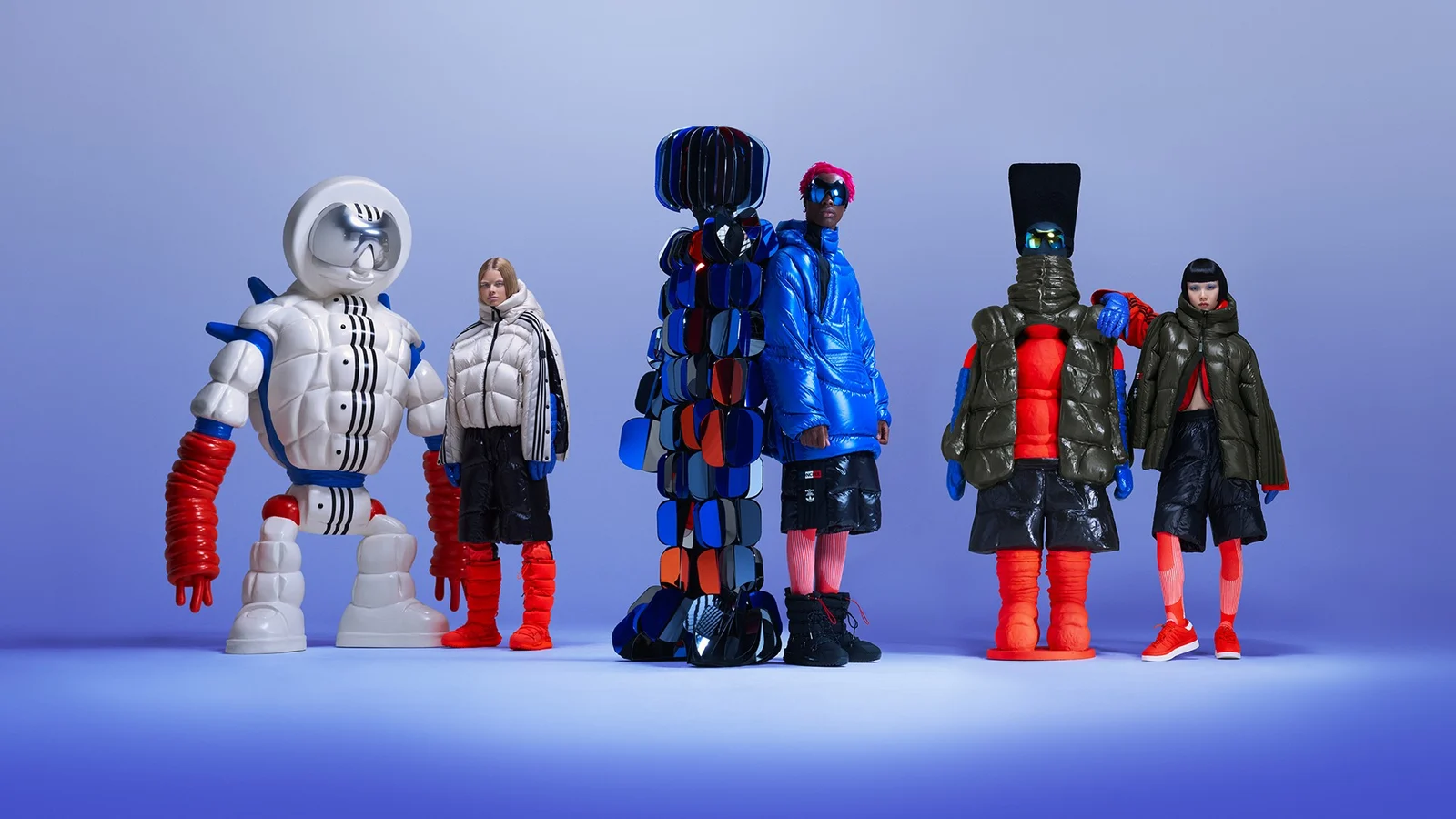 Models and sculptural explorer figures in oversized puffer looks pose against a blue studio backdrop.